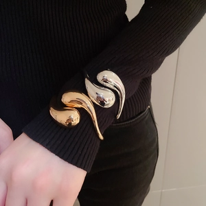 Detailed close-up of gold and silver organic teardrop cuff bracelets over black sleeves