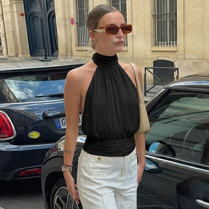 Detail of black halter neck ruched top paired with white trousers on a European street