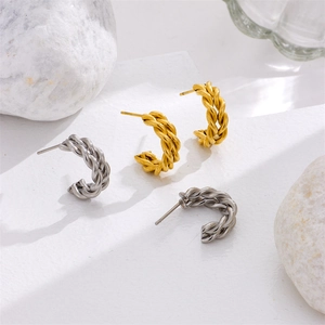 Elegant twisted gold and silver C-shape hoop earrings on a textured stone surface