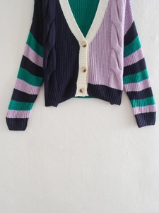 Dettaglio maglia a trecce su cardigan con scollo a V, blocchi colorati e bottoni tartarugati