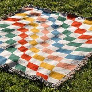 Close-up of geometric checkered woven blanket with tassels on green grass