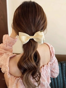 Detail view of large cream satin bow hair claw clip styled on long wavy hair