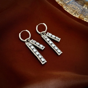 Close-up of geometric silver drop earrings with white crystals on brown satin background