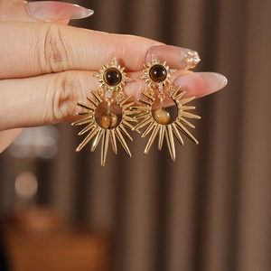 Detail of sunburst earrings with tiger eye stone and zircon held against brown fabric