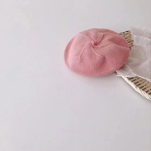 Close-up of pink knitted baby beret hat with soft texture on a white tray