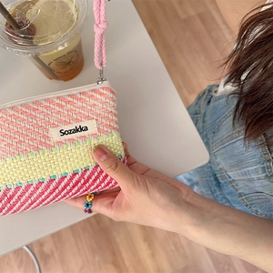 Detail of multi-colored striped woven makeup bag with pink hand strap by Sozakka