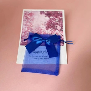 Blue organza gift bag with satin bow on pink background with cherry blossom card detail