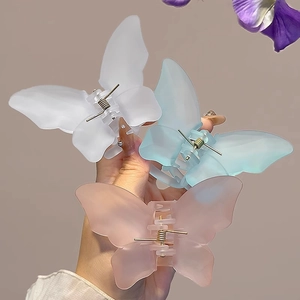 Three matte butterfly hair claws in white, blue, and pink held against floral background