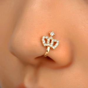 Close-up of a gold-colored crown nose cuff with sparkling rhinestones on human skin