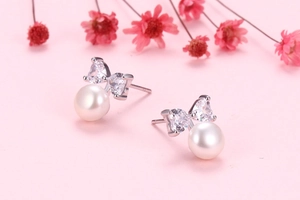 Close-up of bow knot pearl earrings with white zircon accents on a pink floral background
