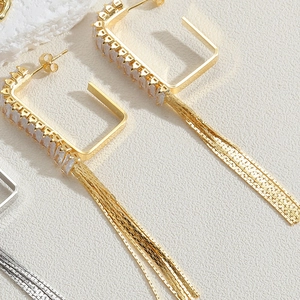 Détail de boucles d'oreilles en U dorées avec zircons carrés et longs glands fins