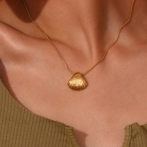Dettaglio di una collana con pendente a conchiglia dorata su catena a serpente indossata