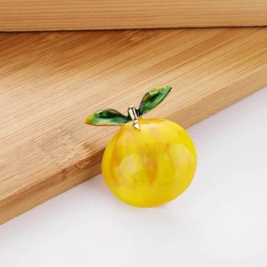 Detailed view of handmade yellow fruit brooch with green leaves and glossy enamel finish