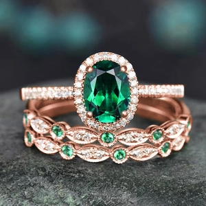 Macro shot of rose gold rings with oval emerald and diamonds on a textured stone surface