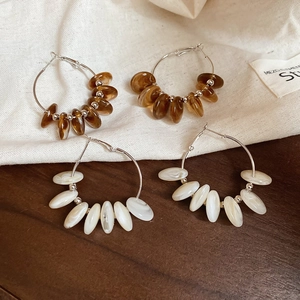 Detail of silver round hoop earrings with brown and white resin beads on a textured fabric