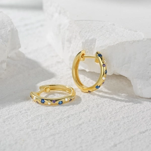 Macro detail of gold hoop earrings with inlaid blue and purple colorful gemstones