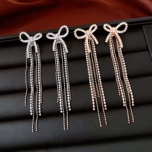 Detail of 18k gold plated bow earrings with dangling rhinestone fringe on black leather