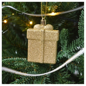 Detail of a golden glitter gift box ornament hanging on a lush green Christmas tree branch