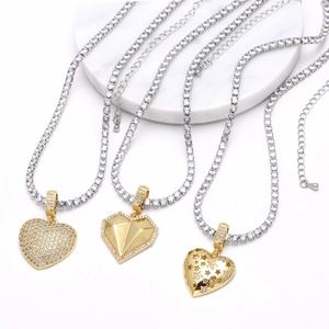Three gold heart pendants on silver diamond tennis chains displayed on marble