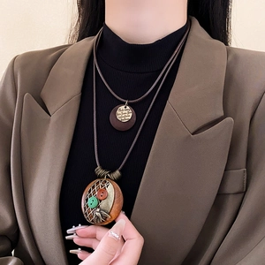 Détail d'un collier double en cuir avec pendentif en bois gravé et accents de bronze