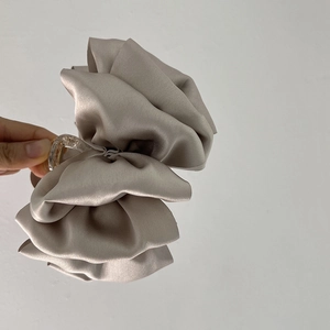 Detail of a large grey satin bow hair claw clip held against a white wall background