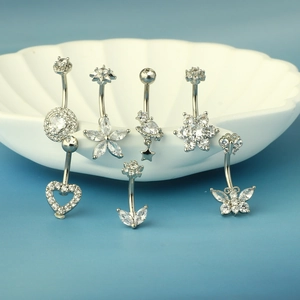 Detail of silver navel rings with cubic zirconia charms on a white shell tray