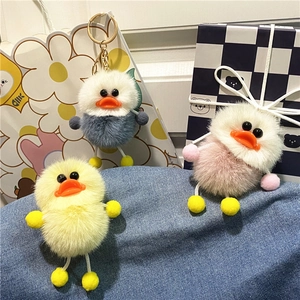 Close-up of cute plush duck keychains in yellow, pink and blue colors on denim cloth