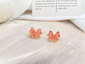 Detail of pink marble bow earrings in gold plating displayed on white silk fabric