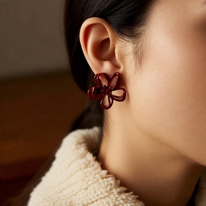 Close-up of deep red hollow flower earrings worn with a beige knitted sweater