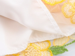 Vue macro de broderie de fleurs jaunes et feuilles vertes sur tissu de robe en tulle