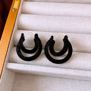 Detailed macro view of black flocked double hoop earrings in a beige jewelry box