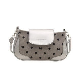 Silver leather handbag with grey polka dot bow and adjustable strap on white backdrop