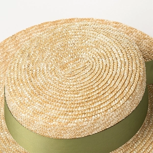 Primo piano di un cappello di paglia a testa piatta con nastro in canneté verde oliva