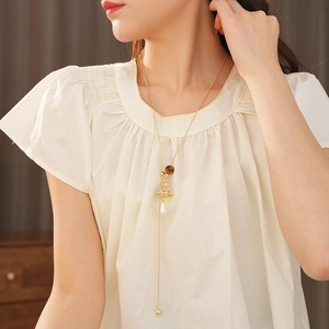 Detailed view of tiger eye stone cross and golden saturn pendant necklace on a model