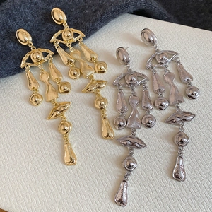 Detail of abstract eye and lip pendant earrings with textured gold and silver finish