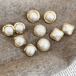 Detailed view of gold geometric pearl earrings on soft brown wool and newspaper background