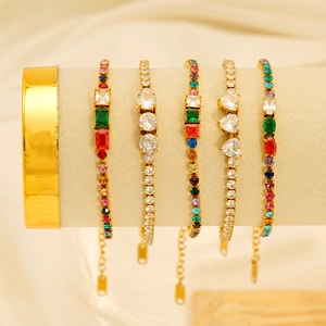 Collezione di bracciali dorati con zirconi colorati su un espositore in tessuto bianco