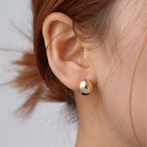 Close-up of a model wearing high-polish gold oval stud earrings with a sleek mirror finish