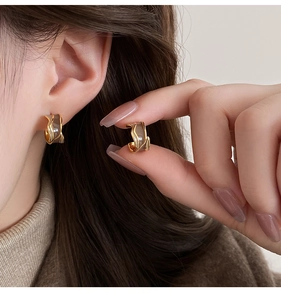 Detail view of C-shaped Maillard drop oil earring on ear and held by hand