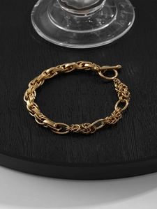 Vue détaillée du bracelet à grosses mailles dorées avec fermoir OT sur socle noir