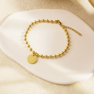 Golden bead bracelet with Elizabeth II coin pendant on a white tray minimalist style