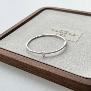 Detail shot of a silver S925 geometric bracelet with a heart-shaped zircon on a linen tray