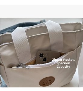 Détail de la poche zippée avant et du logo en cuir marron sur le sac cabas en toile beige