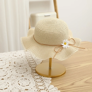 Detail of a beige straw sun hat with wavy brim and daisy flower on a gold stand