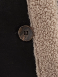 Detail of black fabric with beige faux shearling lining and a brown horn-style button