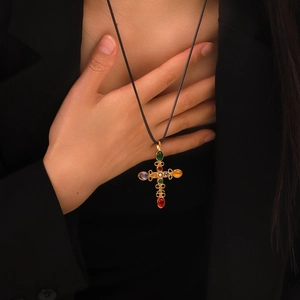 Detail showing a gold cross pendant with colorful gemstones on a black braided cord