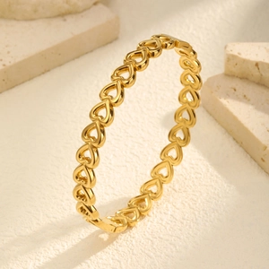 Close-up of gold hollow heart bangle on beige stone background showing metal details