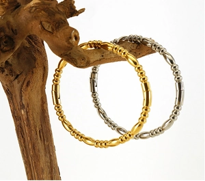 Detail of gold and silver beaded titanium steel bangles on wood branch with side clasp
