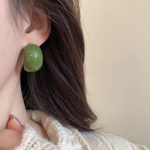 Close-up of a chunky dark green resin C-shape earring worn by a model in a minimal style