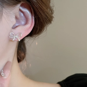Close-up of minimalist silver bow stud earring worn by a model in a natural setting